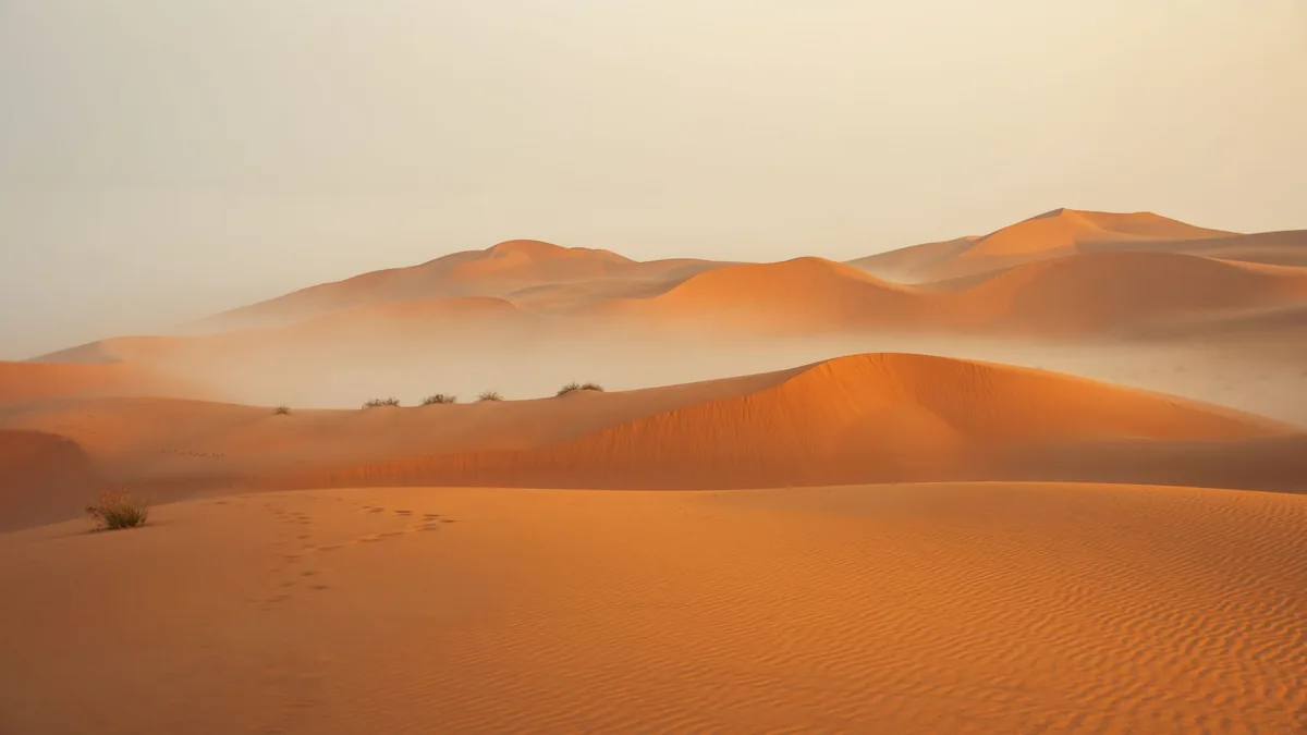 Peaceful desert scene with golden sand dunes and soft mist at sunrise.